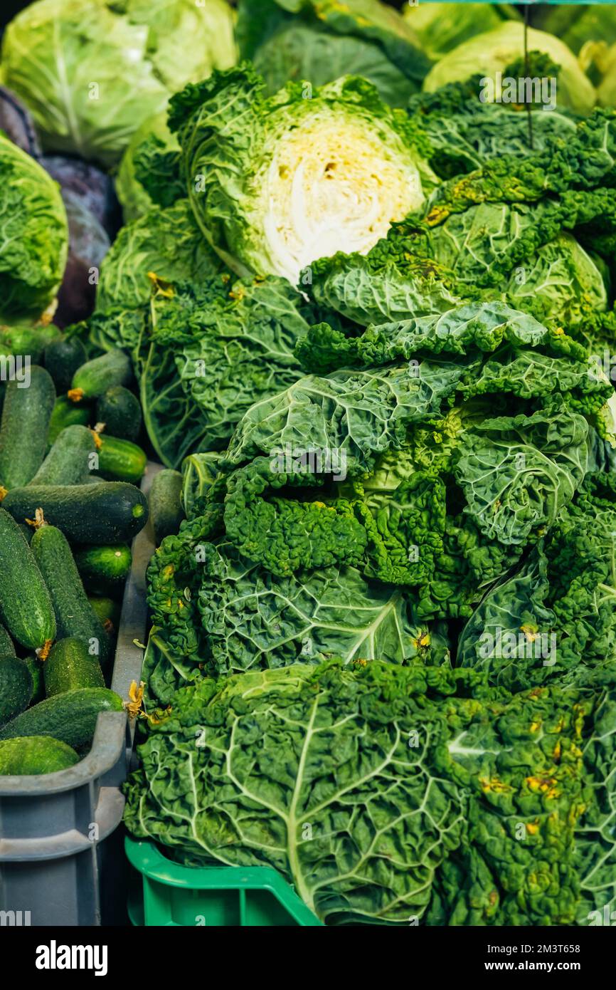 Vertikales Foto von frischen grünen Grünkohl-Blättern und Gurken, die auf einem Markt gedreht wurden. Stockfoto