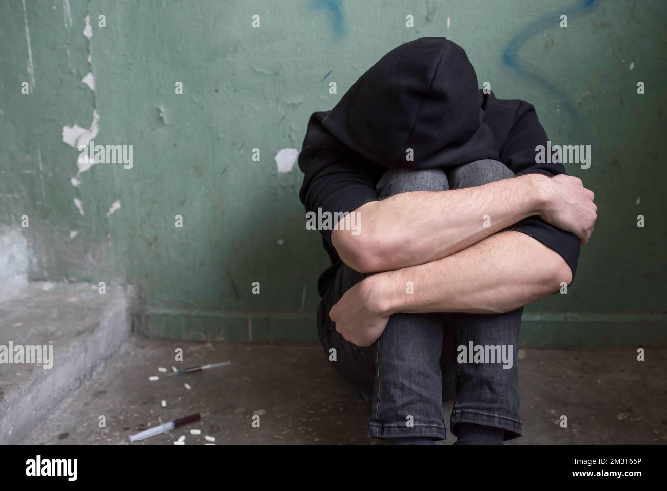 Ein Teenager-Drogenabhängiger sitzt allein, nachdem er Drogen und Alkohol in einem verlassenen Haus konsumiert hat. Suchtbegriff Stockfoto