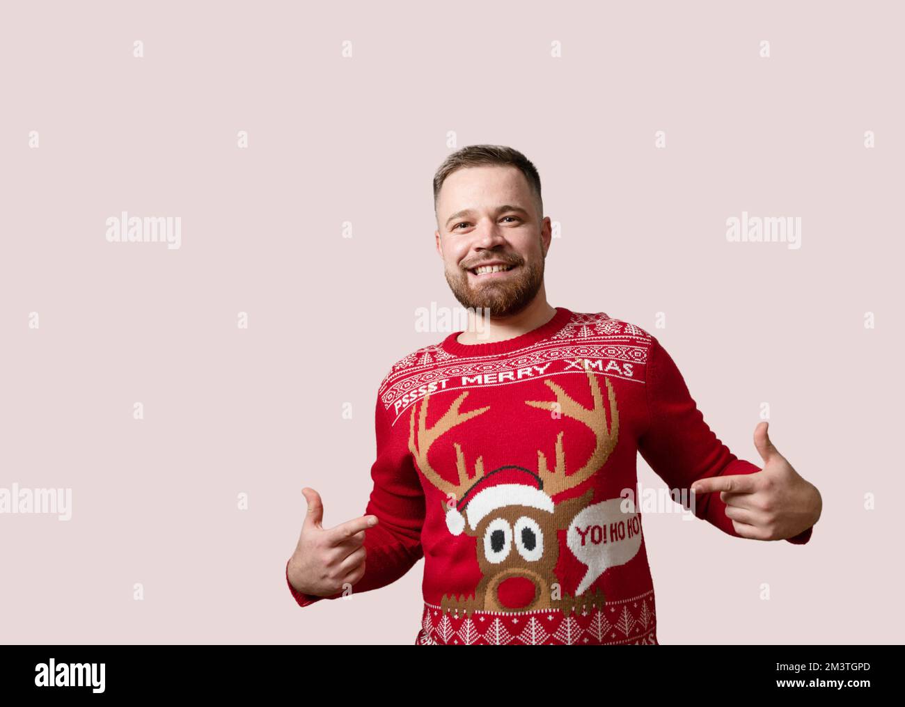 Junger, bärtiger Mann, der seinen Rentier-Weihnachts-Pullover zeigt, isoliert auf rotem Hintergrund. Speicherplatz kopieren Stockfoto