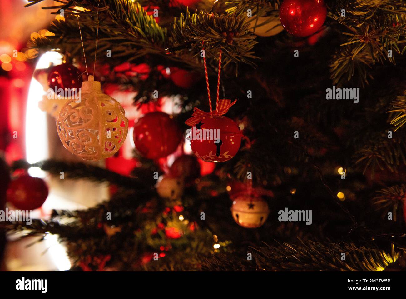 Dekoration des Weihnachtsbaums mit roten Glocken im Vintage-Stil, weiße Kugeln mit Freischnitt. Helle Bokeh-Lichter auf grünem Hintergrund. Dekorati Stockfoto