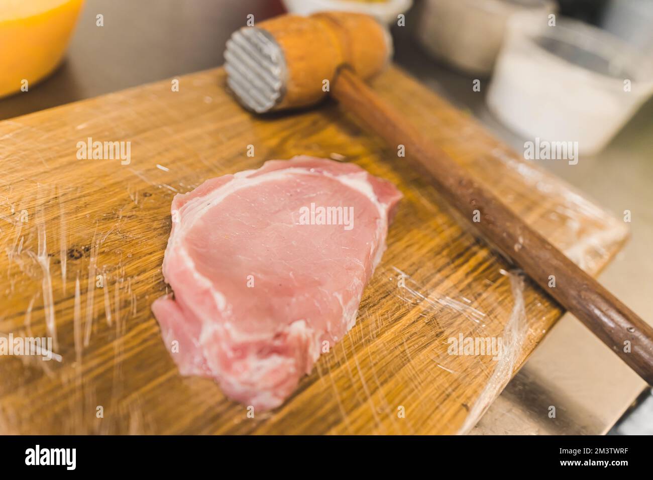 Rohes Schweinekotelett auf Holzbrett. Ein Stück ungekochtes Schweinekotelett neben einem Quirl aus Holz und Metall. Innenaufnahme mit hohem Winkel. Hochwertiges Foto Stockfoto