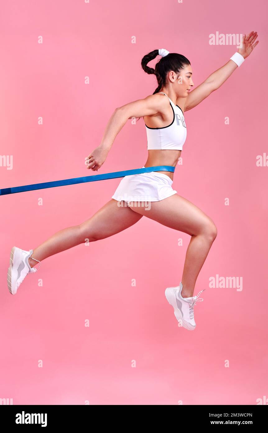 Macht Platz für den Gewinner. Studioaufnahme einer sportlichen jungen Frau, die mit einem Band um die Taille springt und einen pinkfarbenen Hintergrund hat. Stockfoto