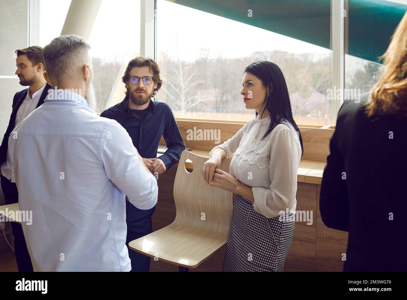 Eine Gruppe von Geschäftsleuten trifft sich in einem modernen Büro, steht am Fenster und spricht Stockfoto