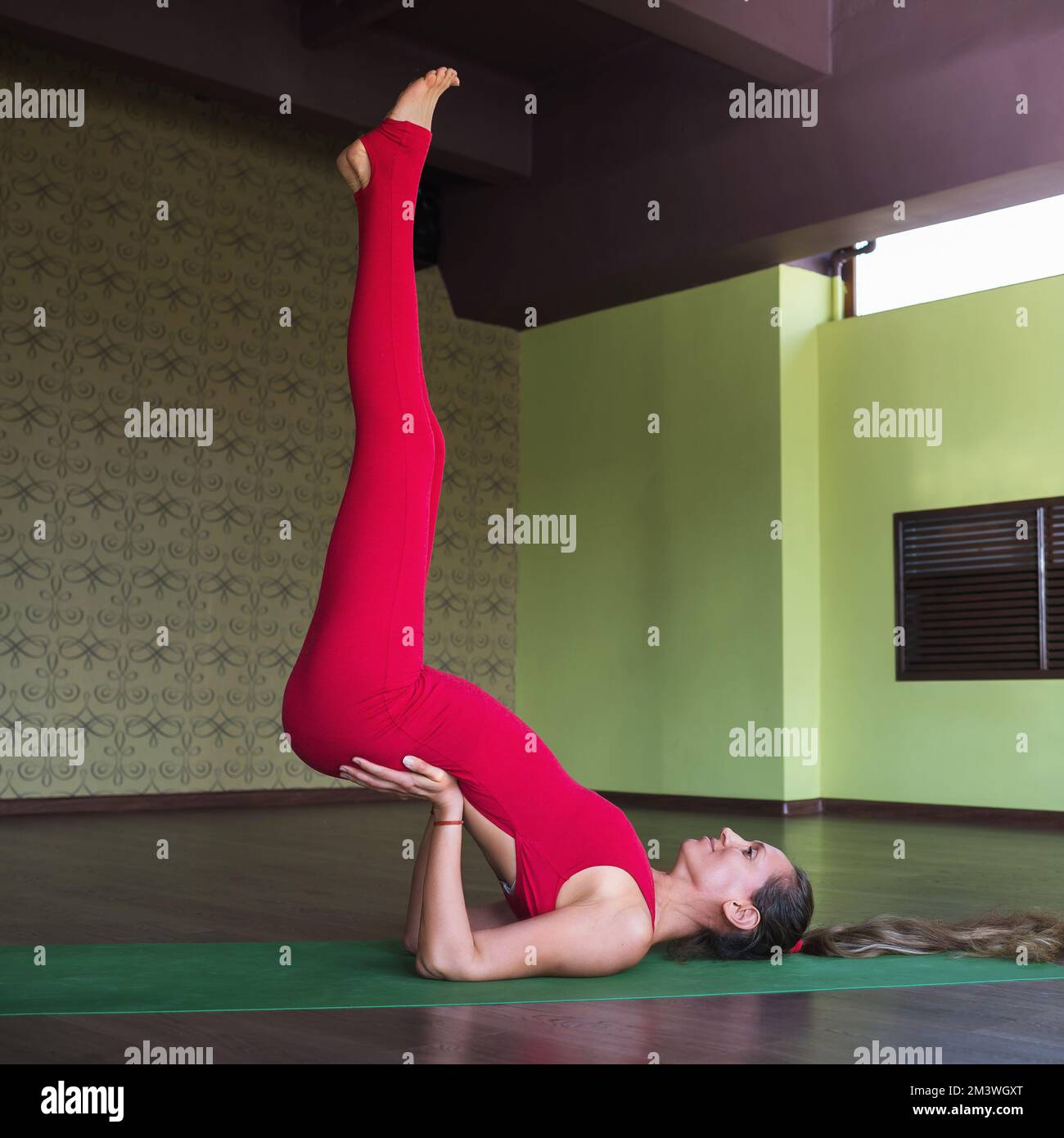 Eine Frau, die einen gesunden Lebensstil führt und Yoga praktiziert, führt eine Variation von Ekapad Pithasans Übung durch, wobei ihre Beine auf dem Kopf stehen, trainieren Stockfoto