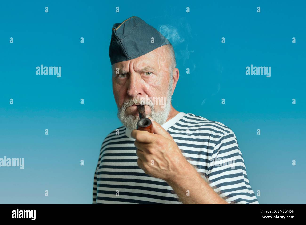 Porträt eines Seemanns in einem gestreiften Hemd und einer blauen Mütze. Ein alter Seemann mit einer Rauchpfeife. Stockfoto