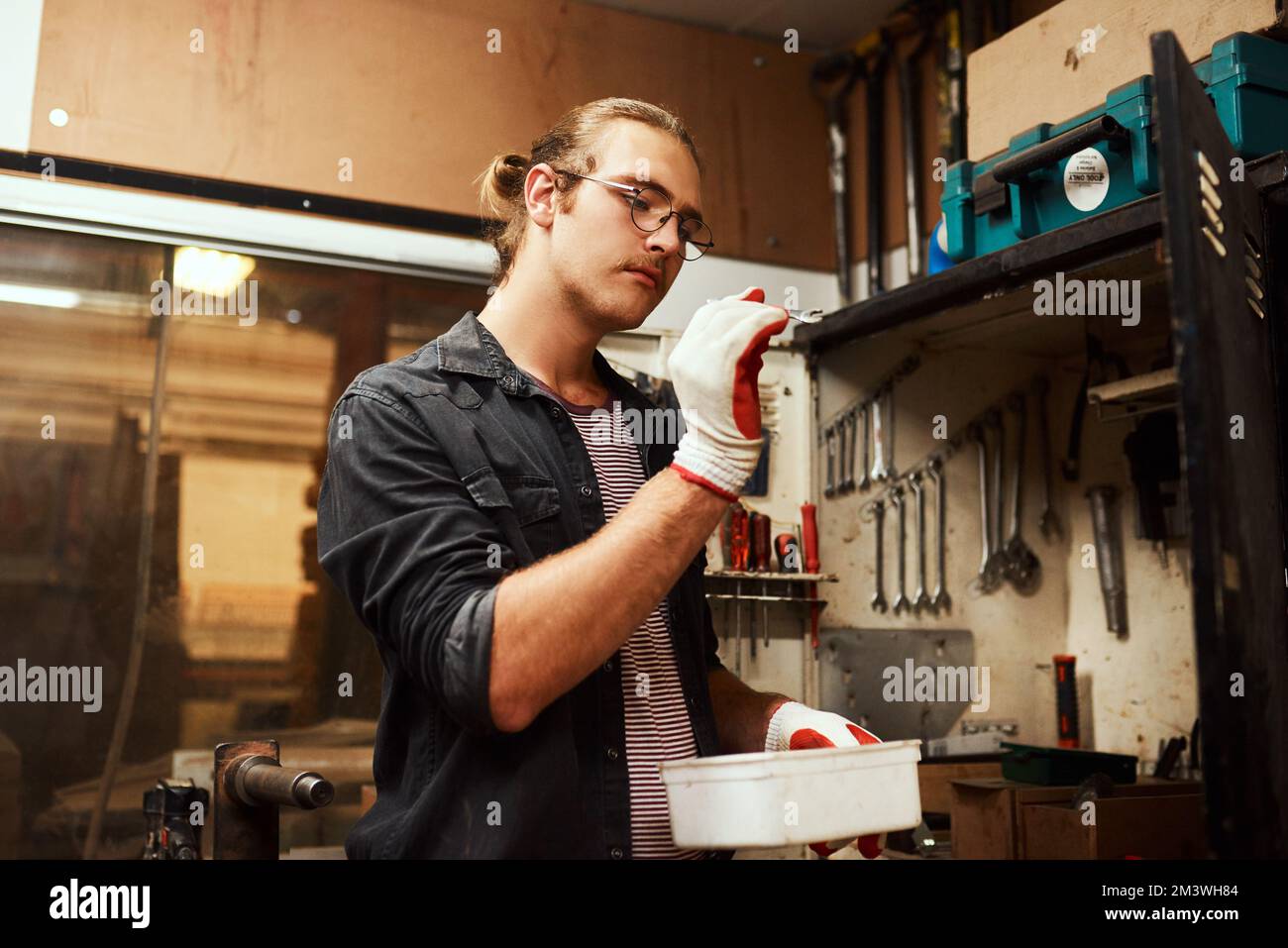Das sollte die richtige Größe haben. Ein fokussierter junger Zimmermann, der einen kleinen Schraubenschlüssel in der Hand hält, um ihn nachts in seiner Werkstatt zu benutzen. Stockfoto