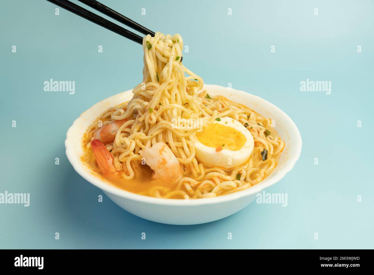 Würzige Suppe nach Thai-Art und Nudeln garniert mit Garnelen, genannt Tom Yum Goong auf weißer Schüssel mit Stäbchen, hergestellt mit Mama-Nudelgarnelen und Chili, heiß Stockfoto