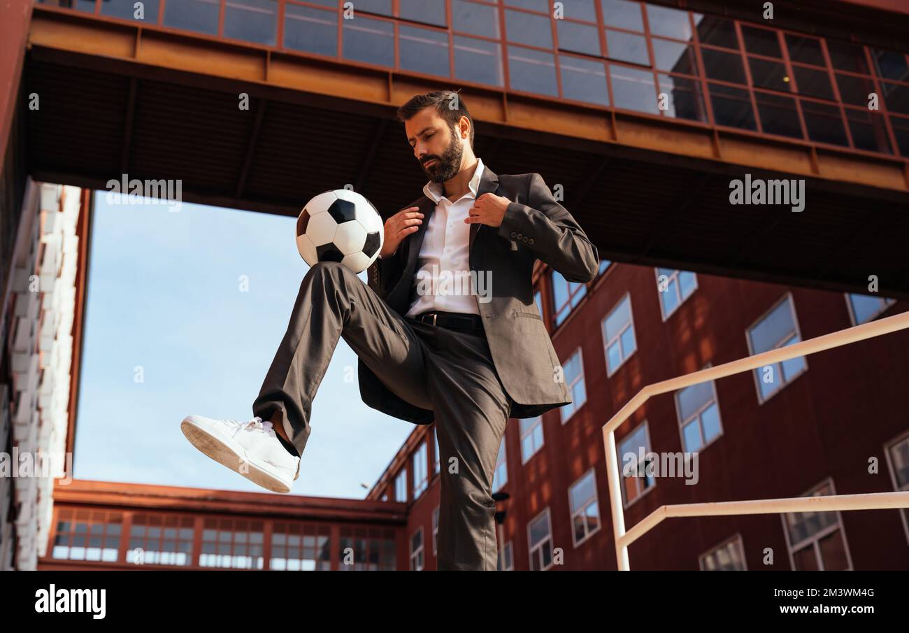 Bild eines Geschäftsmanns und Freispielers, der mit dem Ball auf der Straße Tricks macht. Konzept über Sport- und Geschäftsleute Stockfoto