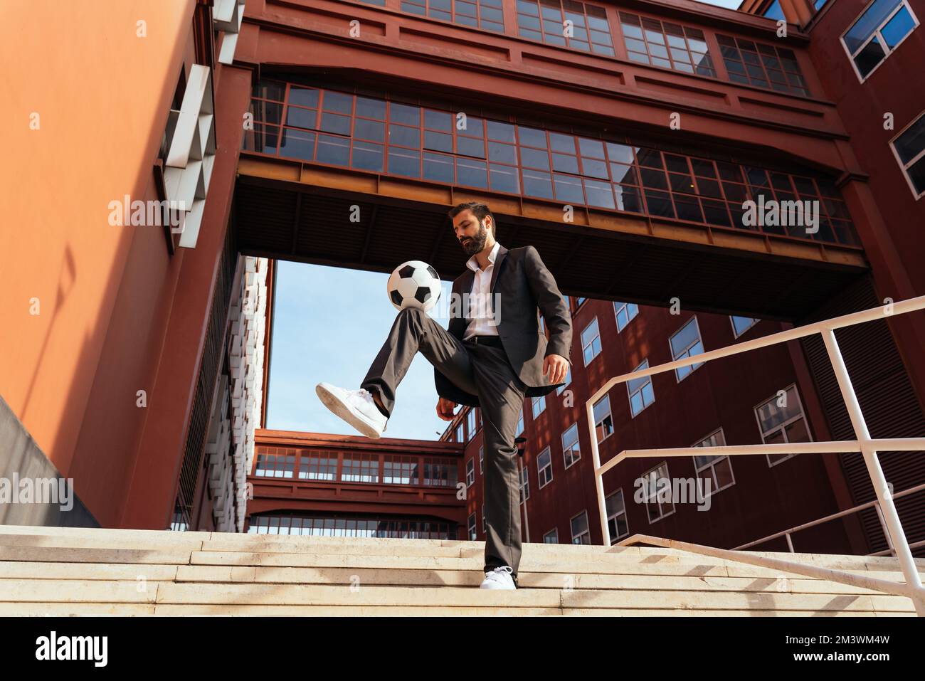 Bild eines Geschäftsmanns und Freispielers, der mit dem Ball auf der Straße Tricks macht. Konzept über Sport- und Geschäftsleute Stockfoto
