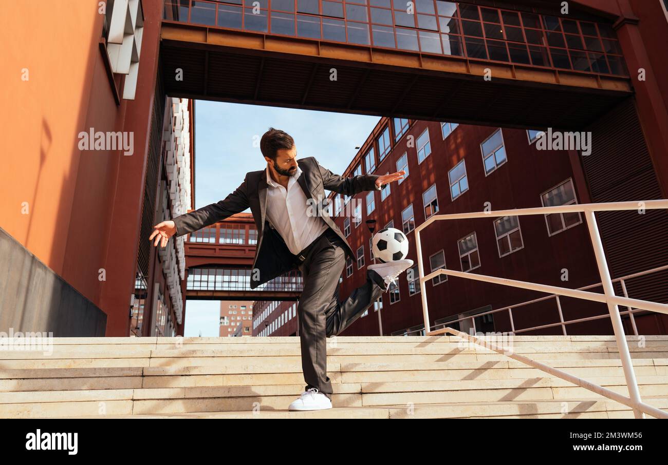 Bild eines Geschäftsmanns und Freispielers, der mit dem Ball auf der Straße Tricks macht. Konzept über Sport- und Geschäftsleute Stockfoto