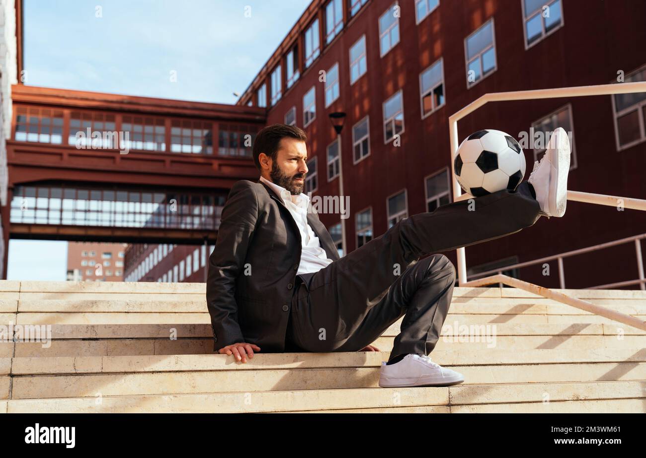 Bild eines Geschäftsmanns und Freispielers, der mit dem Ball auf der Straße Tricks macht. Konzept über Sport- und Geschäftsleute Stockfoto