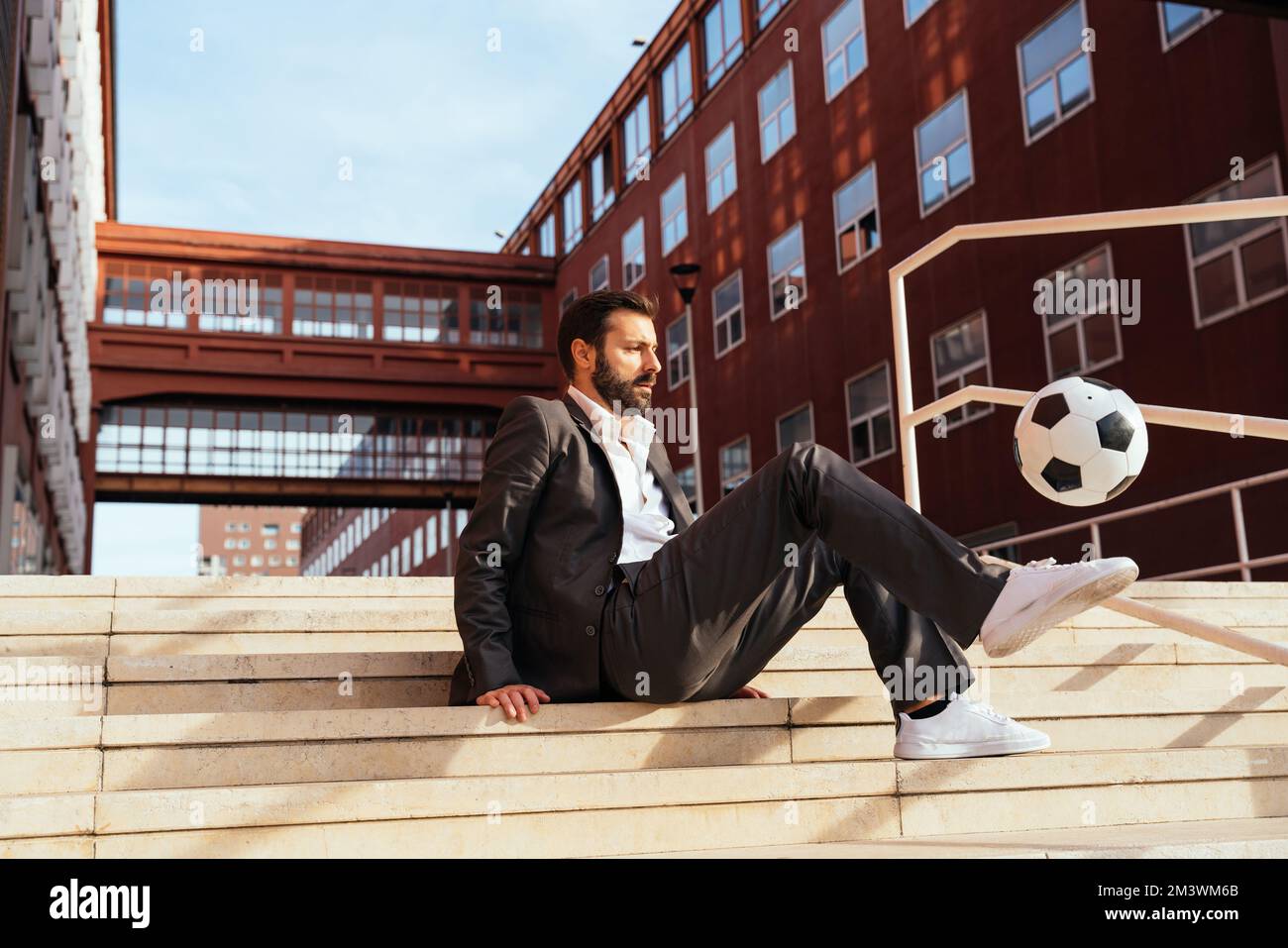 Bild eines Geschäftsmanns und Freispielers, der mit dem Ball auf der Straße Tricks macht. Konzept über Sport- und Geschäftsleute Stockfoto