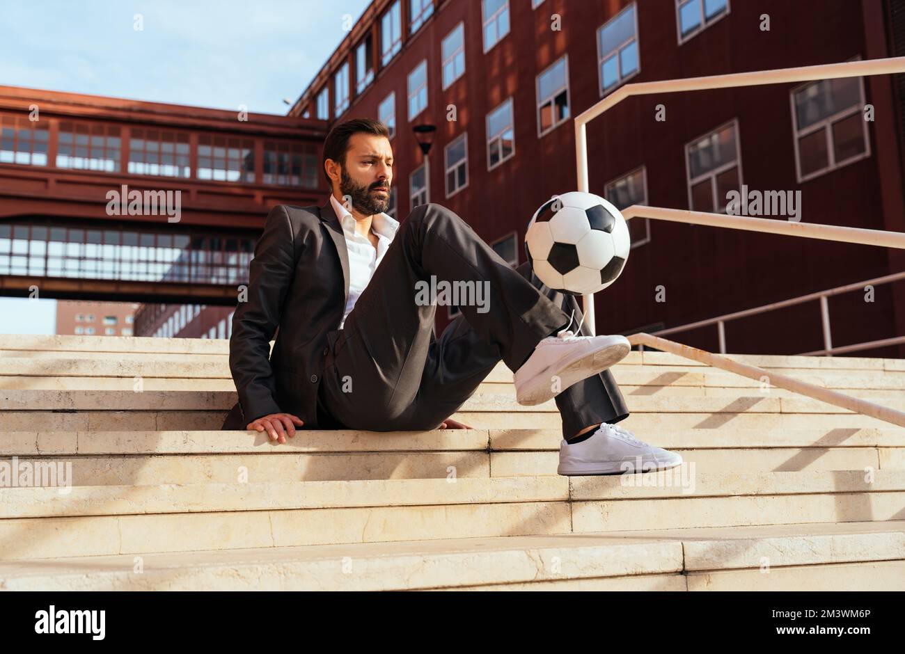 Bild eines Geschäftsmanns und Freispielers, der mit dem Ball auf der Straße Tricks macht. Konzept über Sport- und Geschäftsleute Stockfoto