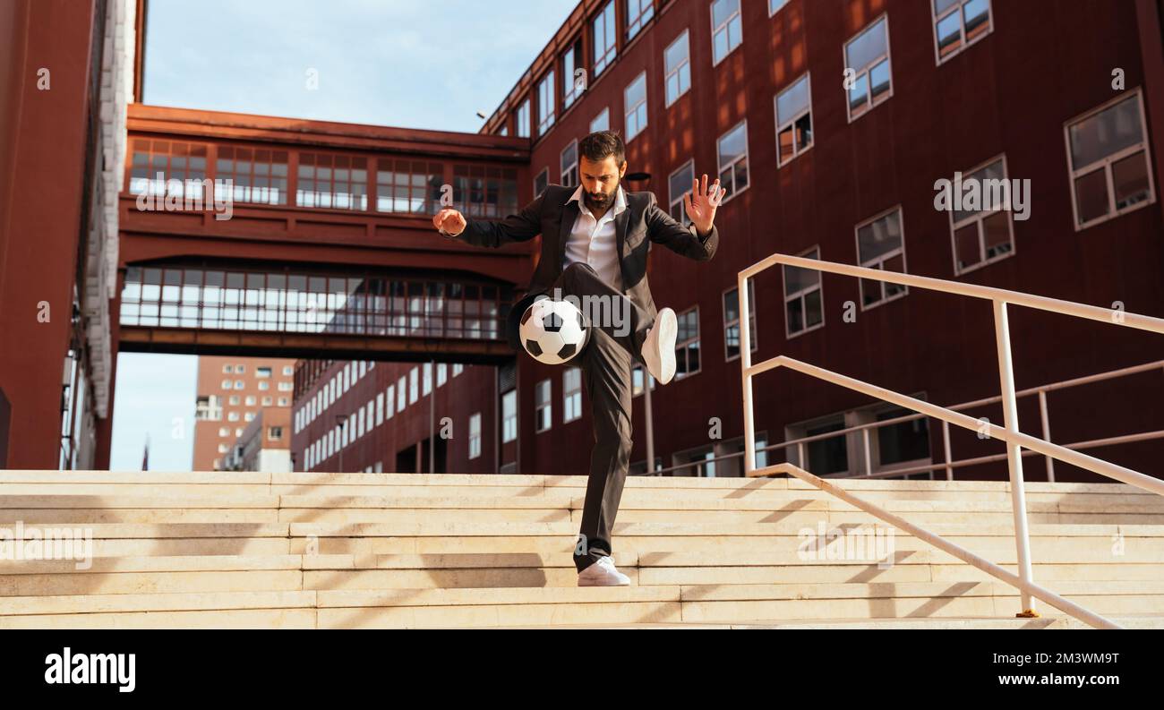 Bild eines Geschäftsmanns und Freispielers, der mit dem Ball auf der Straße Tricks macht. Konzept über Sport- und Geschäftsleute Stockfoto