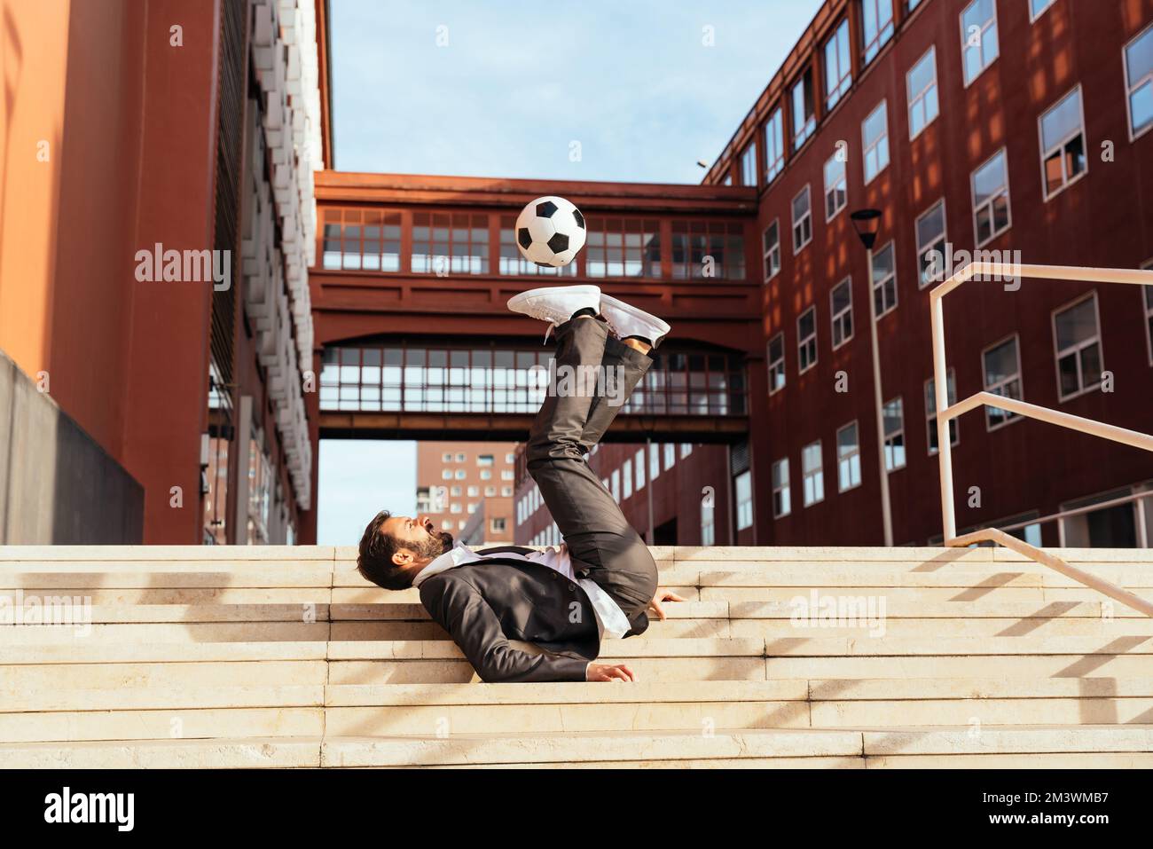 Bild eines Geschäftsmanns und Freispielers, der mit dem Ball auf der Straße Tricks macht. Konzept über Sport- und Geschäftsleute Stockfoto