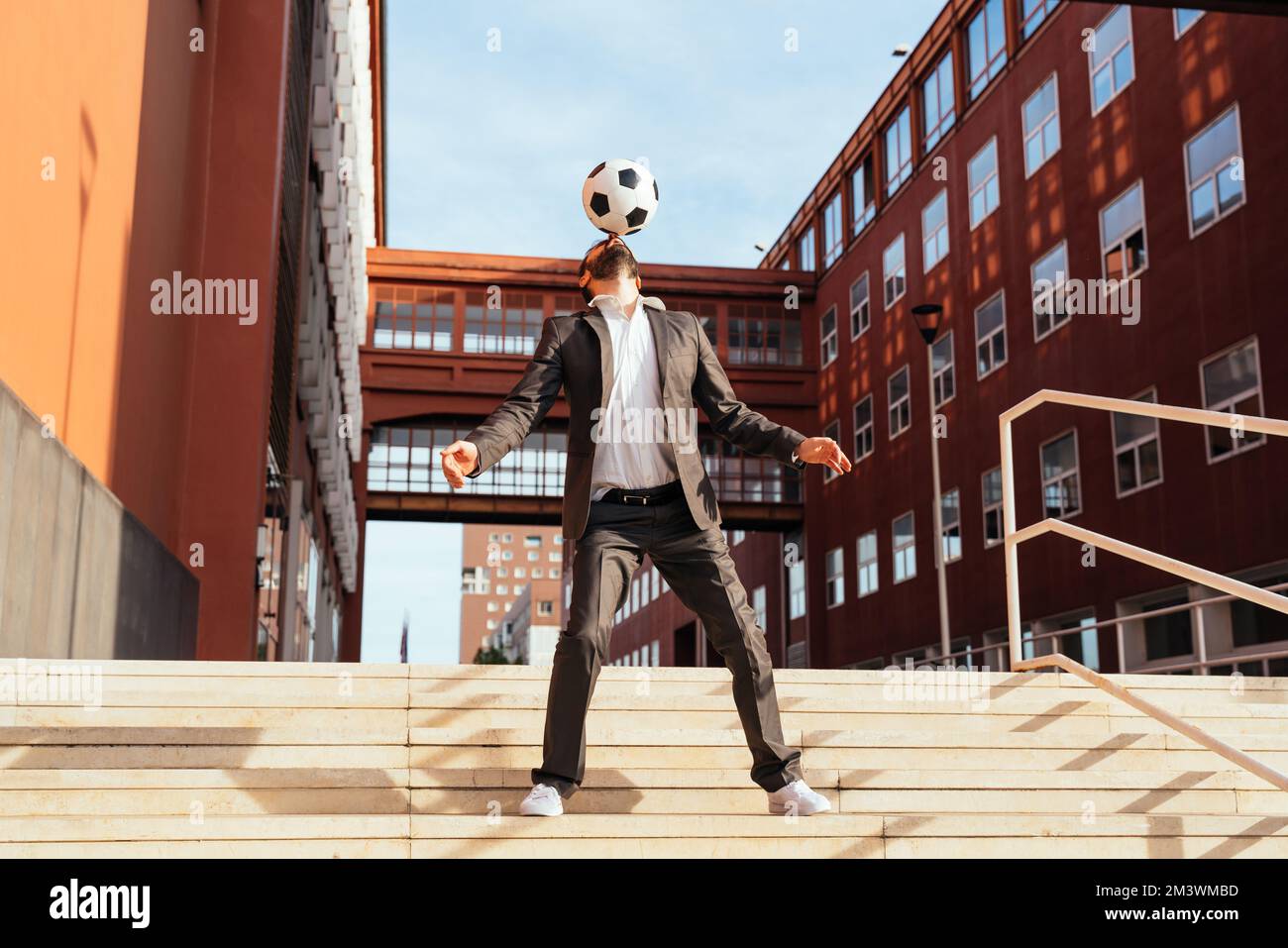 Bild eines Geschäftsmanns und Freispielers, der mit dem Ball auf der Straße Tricks macht. Konzept über Sport- und Geschäftsleute Stockfoto