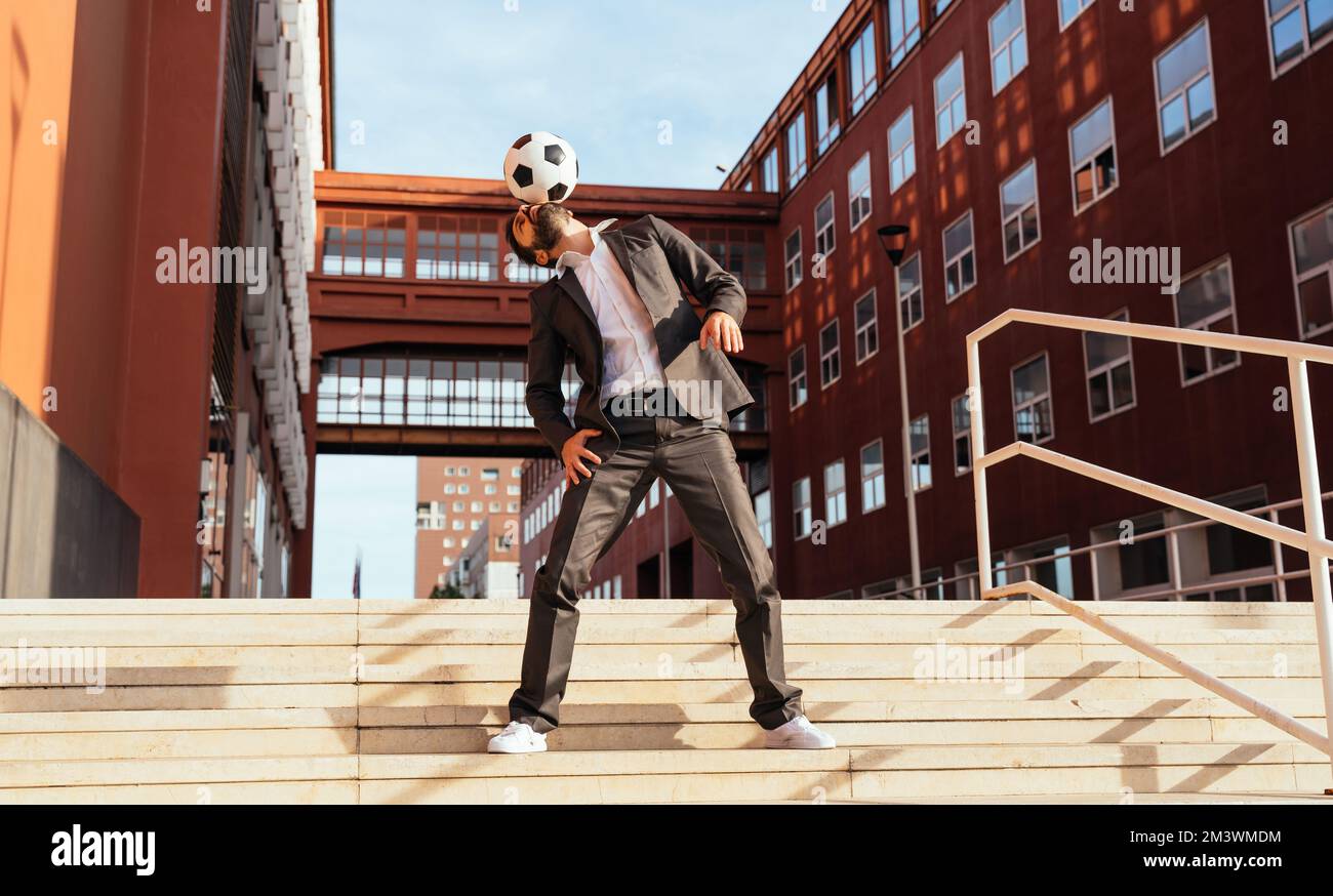 Bild eines Geschäftsmanns und Freispielers, der mit dem Ball auf der Straße Tricks macht. Konzept über Sport- und Geschäftsleute Stockfoto