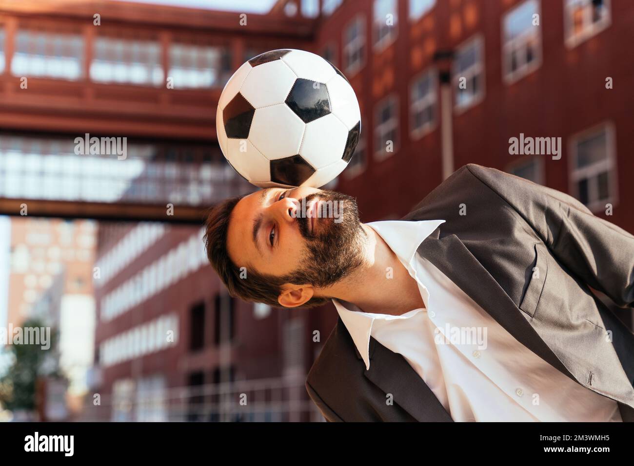 Bild eines Geschäftsmanns und Freispielers, der mit dem Ball auf der Straße Tricks macht. Konzept über Sport- und Geschäftsleute Stockfoto