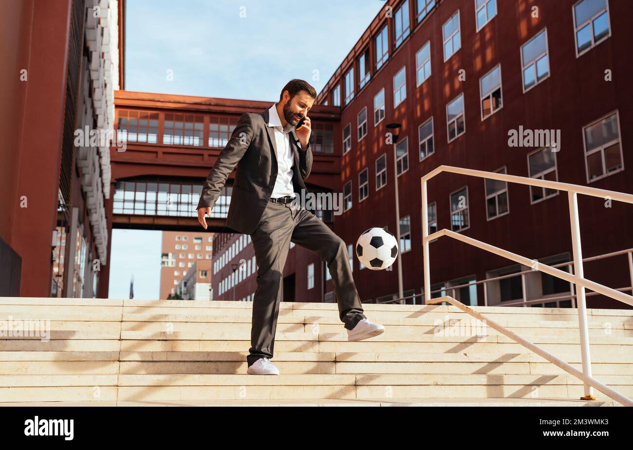 Bild eines Geschäftsmanns und Freispielers, der mit dem Ball auf der Straße Tricks macht. Konzept über Sport- und Geschäftsleute Stockfoto