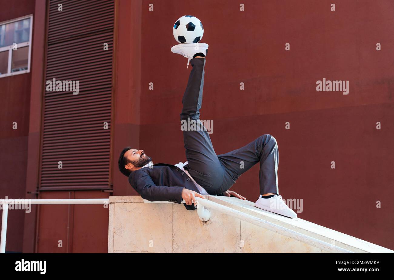 Bild eines Geschäftsmanns und Freispielers, der mit dem Ball auf der Straße Tricks macht. Konzept über Sport- und Geschäftsleute Stockfoto