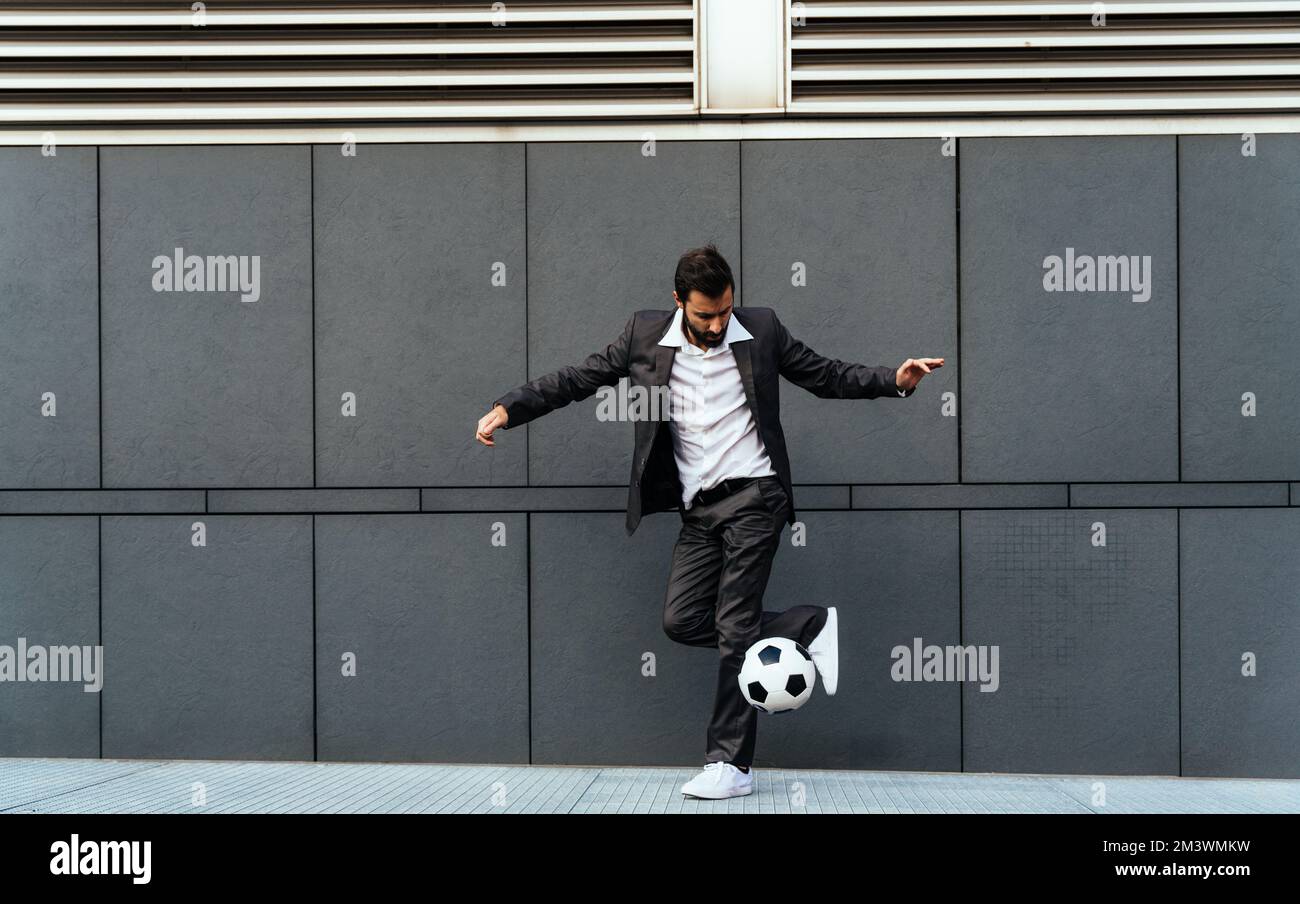 Bild eines Geschäftsmanns und Freispielers, der mit dem Ball auf der Straße Tricks macht. Konzept über Sport- und Geschäftsleute Stockfoto