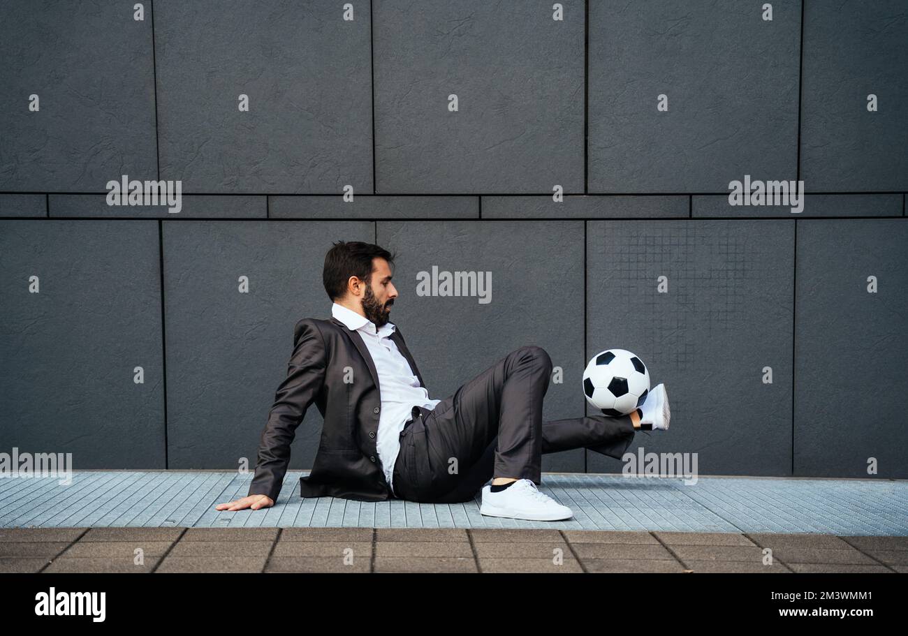 Bild eines Geschäftsmanns und Freispielers, der mit dem Ball auf der Straße Tricks macht. Konzept über Sport- und Geschäftsleute Stockfoto