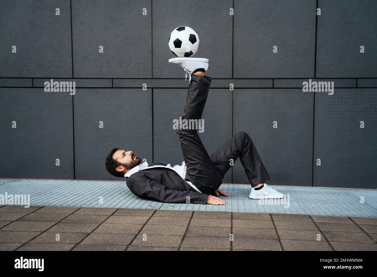Bild eines Geschäftsmanns und Freispielers, der mit dem Ball auf der Straße Tricks macht. Konzept über Sport- und Geschäftsleute Stockfoto