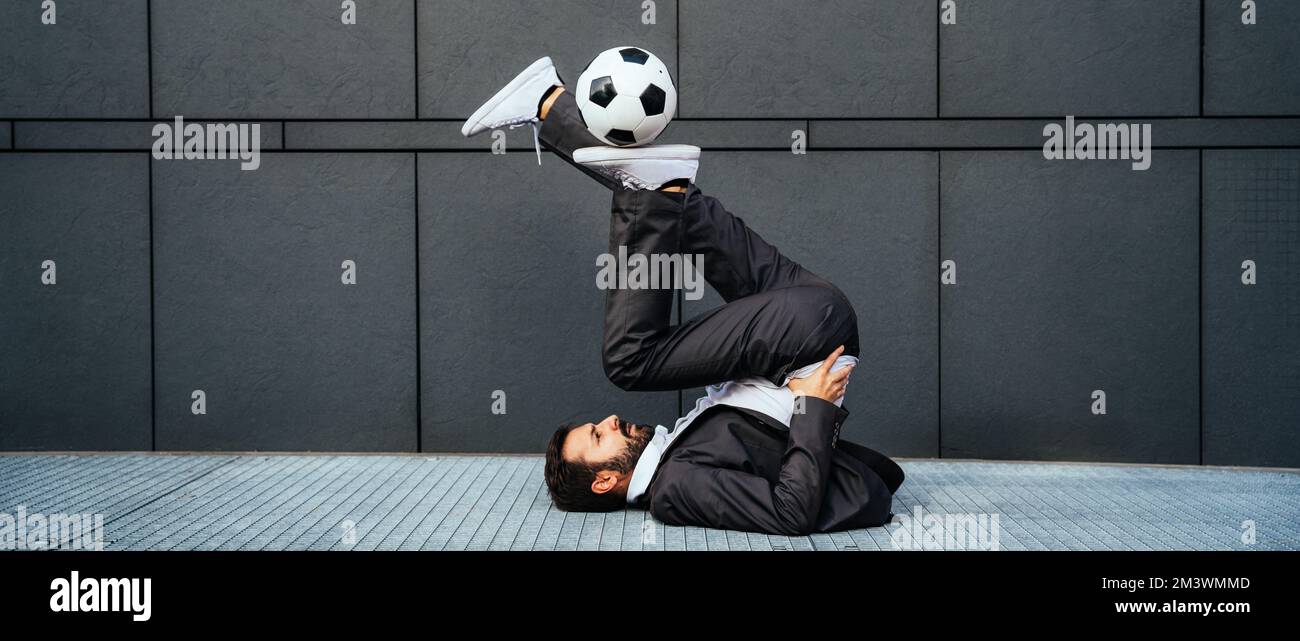 Bild eines Geschäftsmanns und Freispielers, der mit dem Ball auf der Straße Tricks macht. Konzept über Sport- und Geschäftsleute Stockfoto