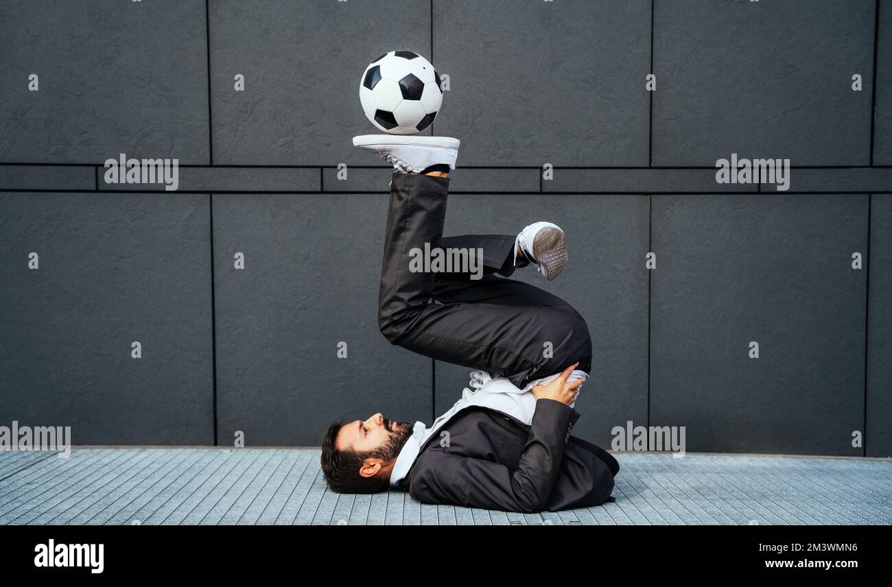 Bild eines Geschäftsmanns und Freispielers, der mit dem Ball auf der Straße Tricks macht. Konzept über Sport- und Geschäftsleute Stockfoto