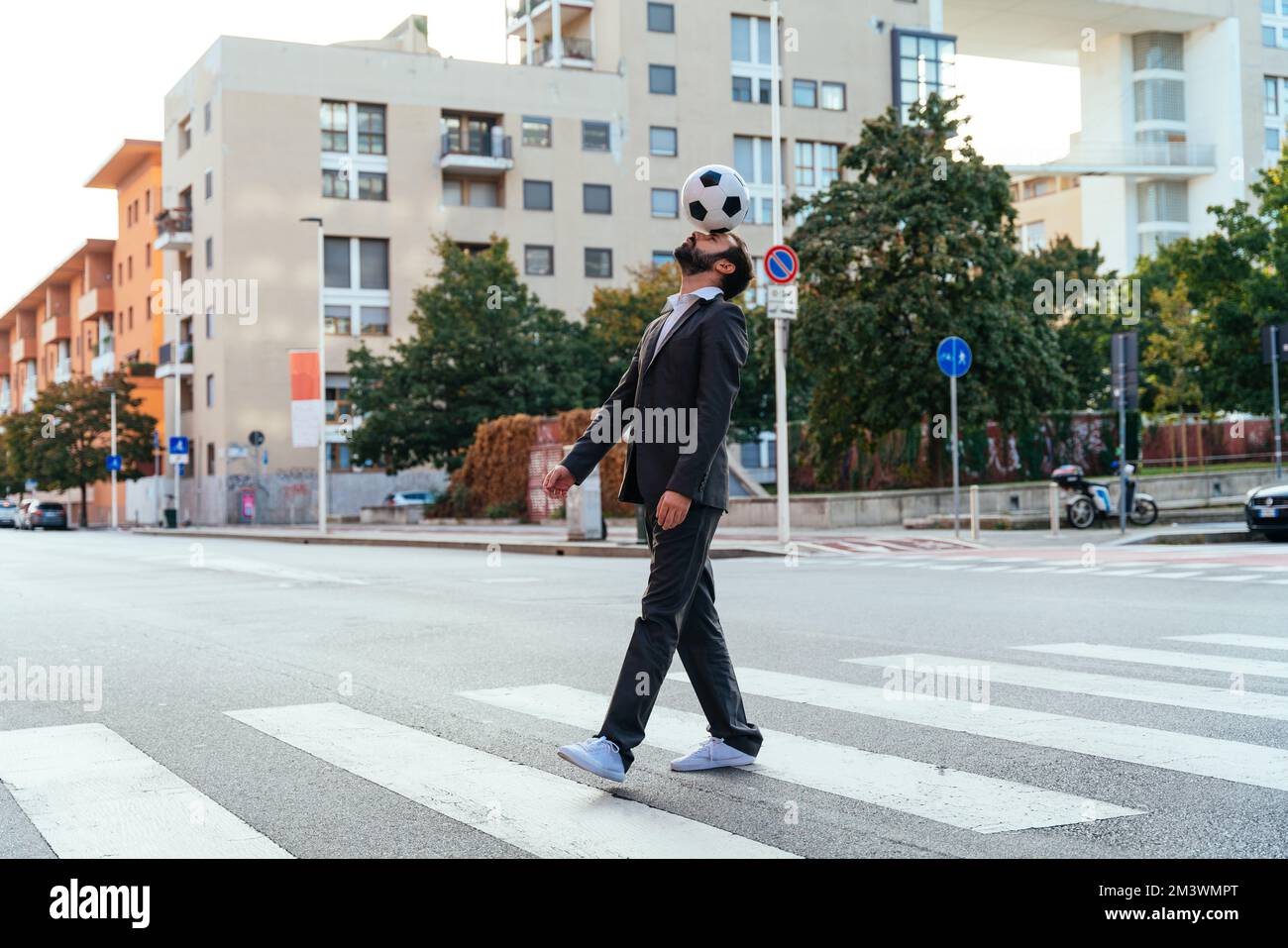 Bild eines Geschäftsmanns und Freispielers, der mit dem Ball auf der Straße Tricks macht. Konzept über Sport- und Geschäftsleute Stockfoto