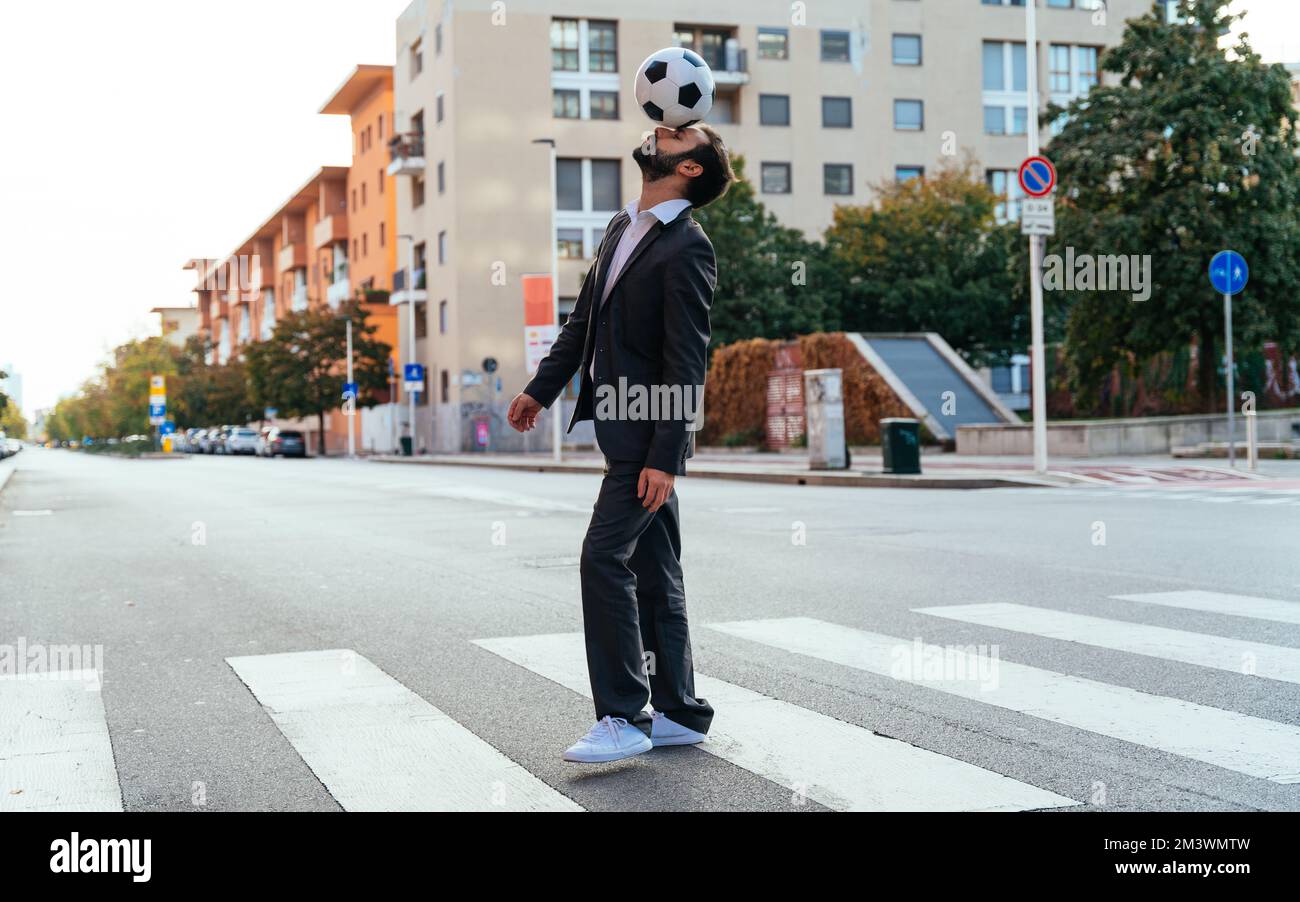 Bild eines Geschäftsmanns und Freispielers, der mit dem Ball auf der Straße Tricks macht. Konzept über Sport- und Geschäftsleute Stockfoto