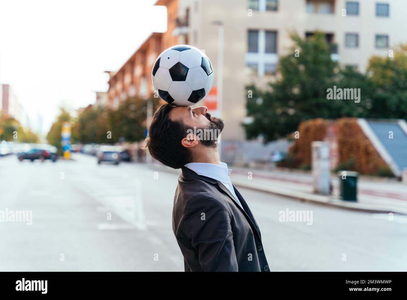 Bild eines Geschäftsmanns und Freispielers, der mit dem Ball auf der Straße Tricks macht. Konzept über Sport- und Geschäftsleute Stockfoto