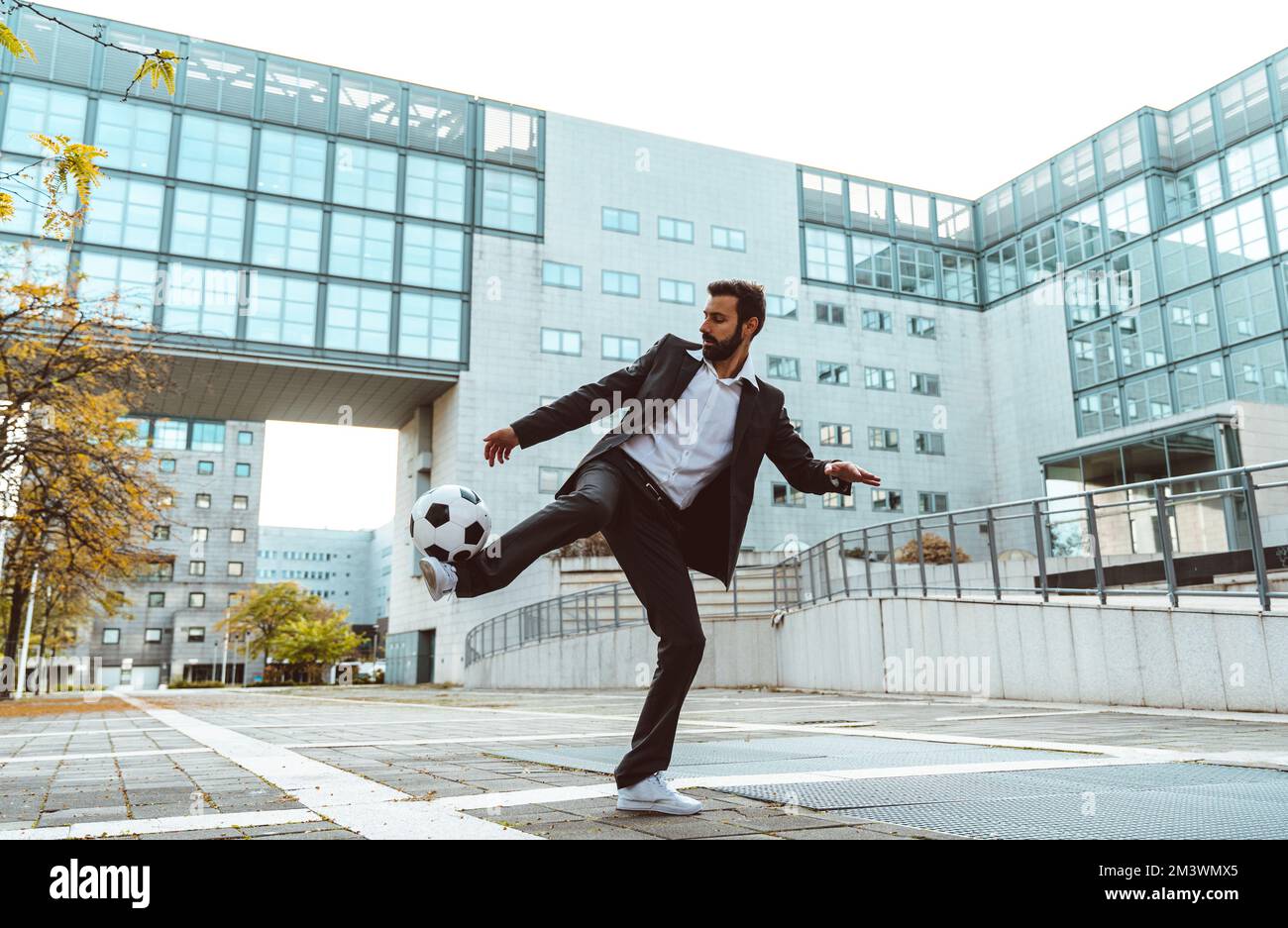 Bild eines Geschäftsmanns und Freispielers, der mit dem Ball auf der Straße Tricks macht. Konzept über Sport- und Geschäftsleute Stockfoto