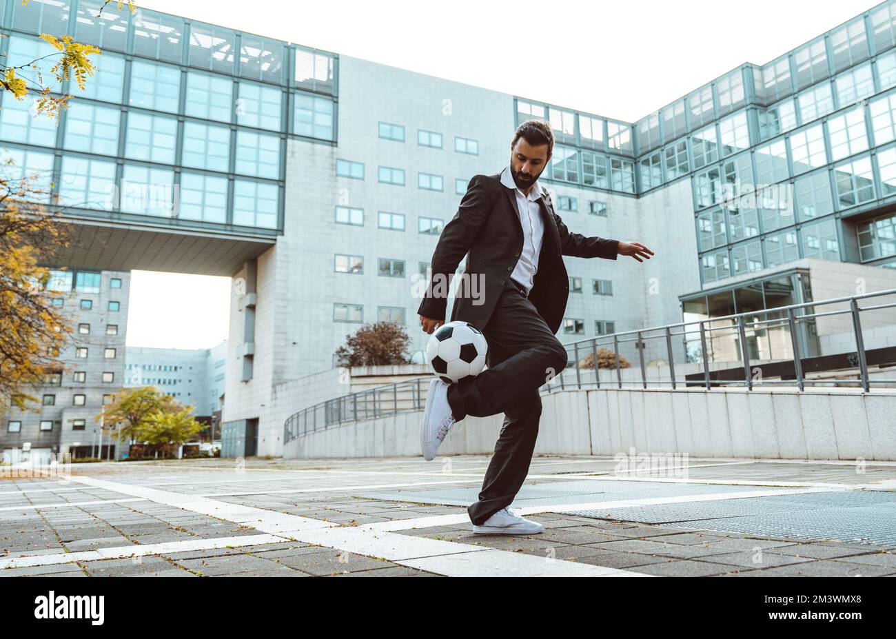Bild eines Geschäftsmanns und Freispielers, der mit dem Ball auf der Straße Tricks macht. Konzept über Sport- und Geschäftsleute Stockfoto