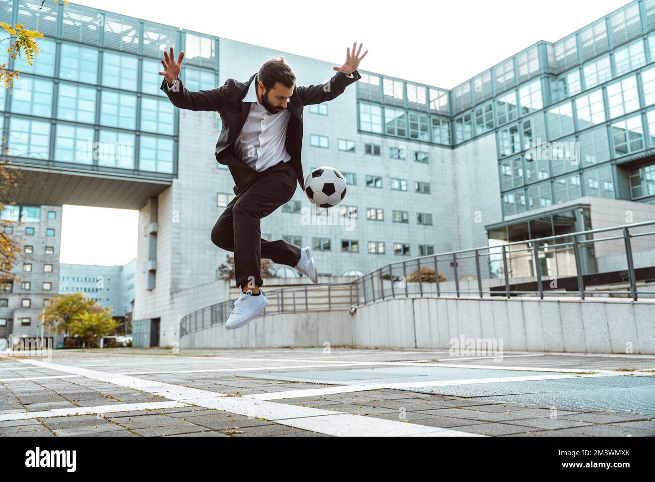 Bild eines Geschäftsmanns und Freispielers, der mit dem Ball auf der Straße Tricks macht. Konzept über Sport- und Geschäftsleute Stockfoto