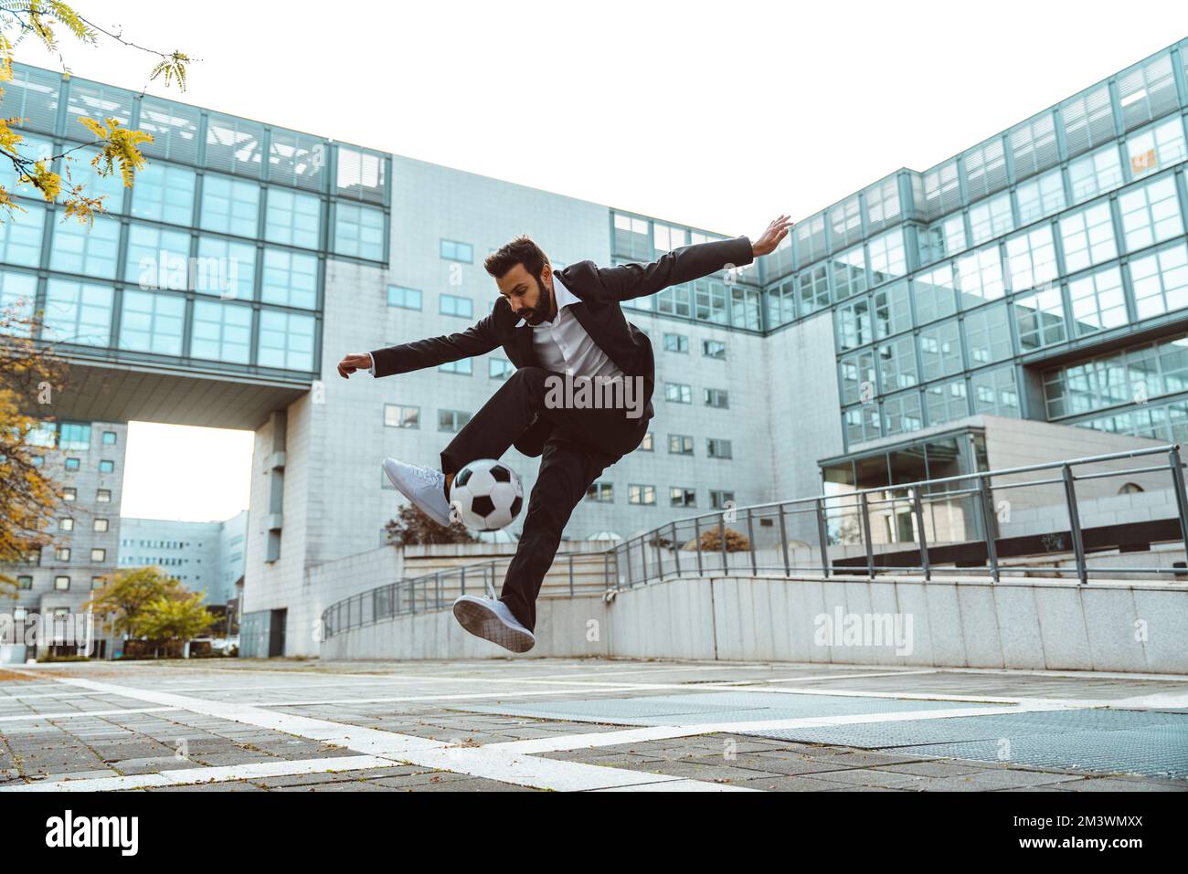 Bild eines Geschäftsmanns und Freispielers, der mit dem Ball auf der Straße Tricks macht. Konzept über Sport- und Geschäftsleute Stockfoto