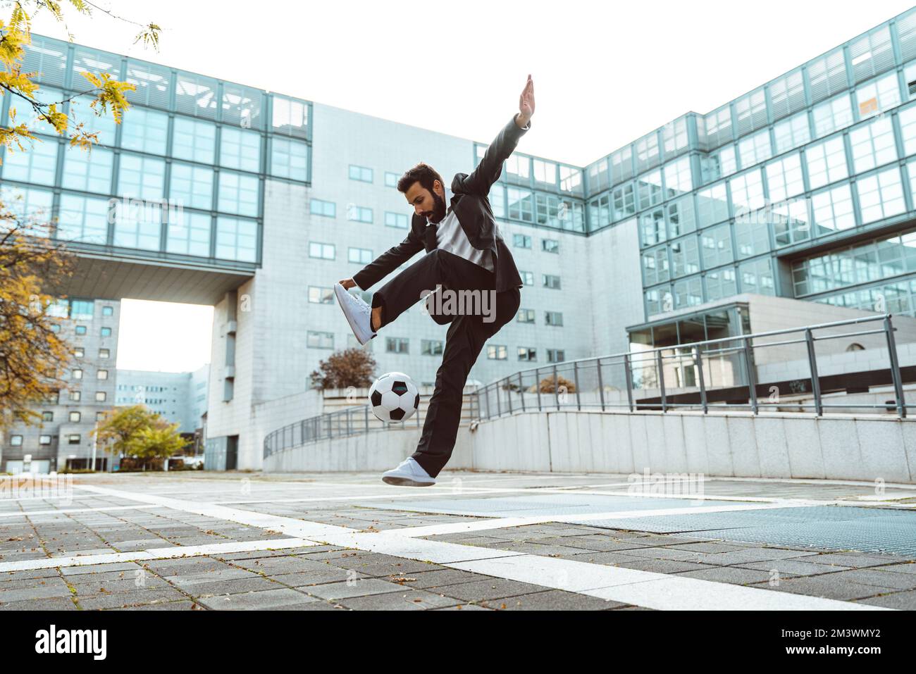 Bild eines Geschäftsmanns und Freispielers, der mit dem Ball auf der Straße Tricks macht. Konzept über Sport- und Geschäftsleute Stockfoto