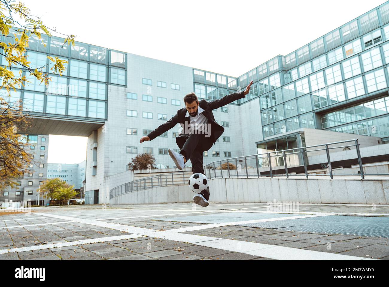 Bild eines Geschäftsmanns und Freispielers, der mit dem Ball auf der Straße Tricks macht. Konzept über Sport- und Geschäftsleute Stockfoto