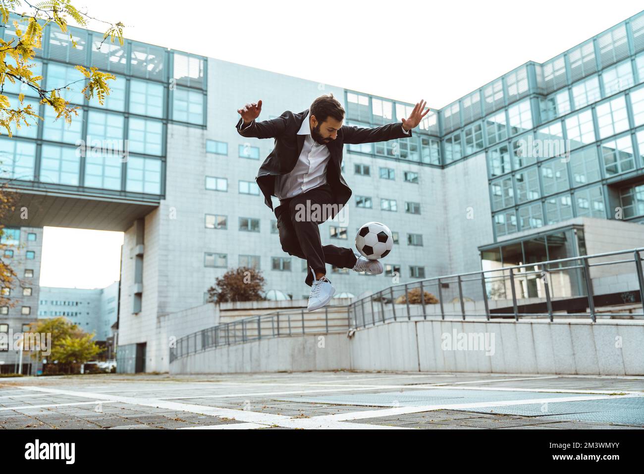 Bild eines Geschäftsmanns und Freispielers, der mit dem Ball auf der Straße Tricks macht. Konzept über Sport- und Geschäftsleute Stockfoto