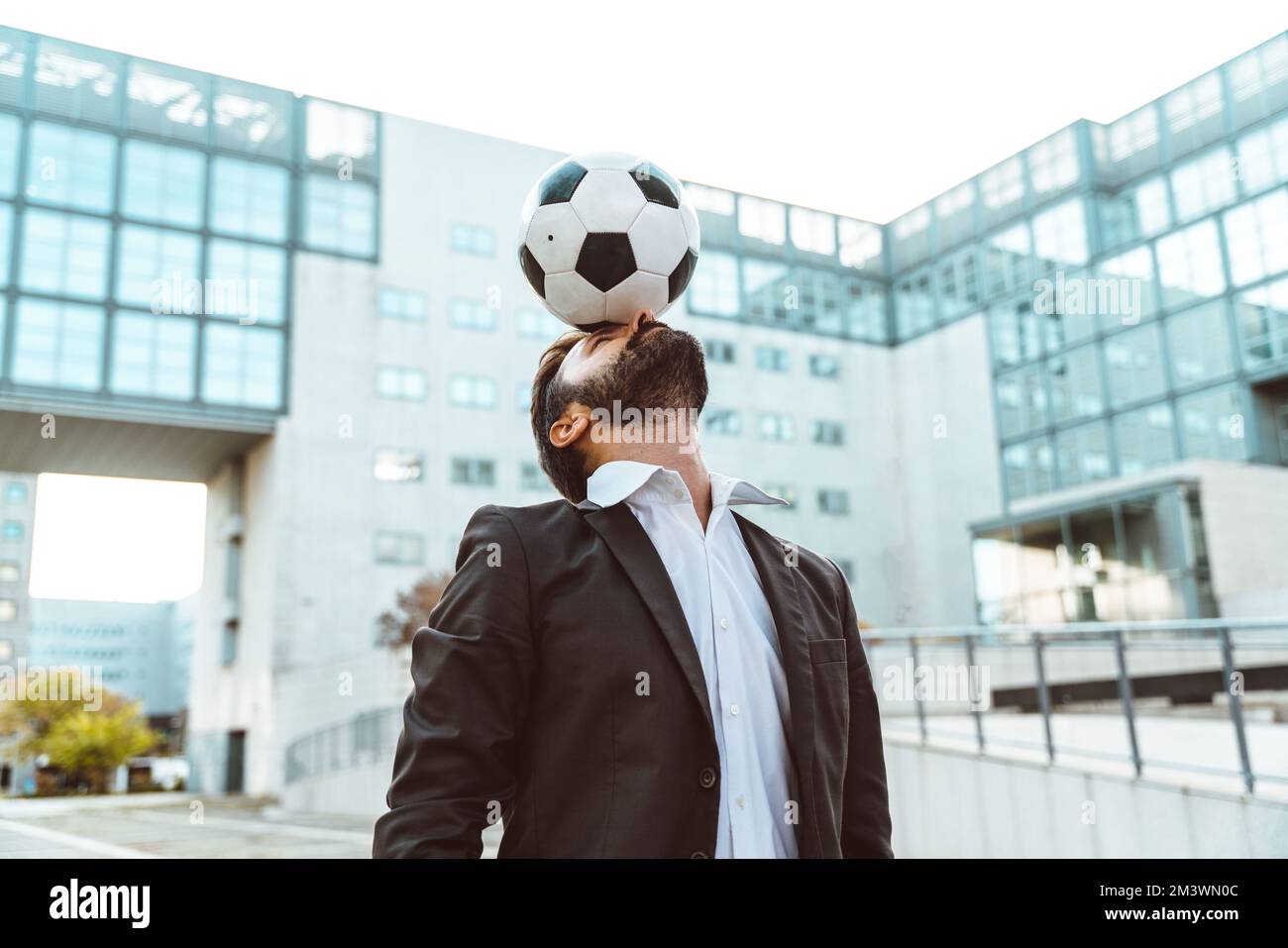 Bild eines Geschäftsmanns und Freispielers, der mit dem Ball auf der Straße Tricks macht. Konzept über Sport- und Geschäftsleute Stockfoto
