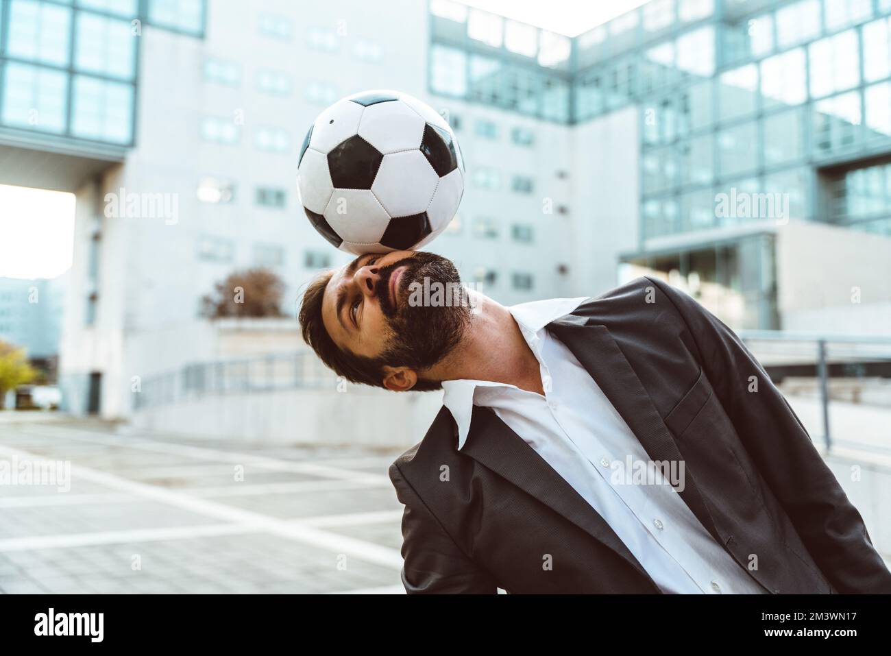 Bild eines Geschäftsmanns und Freispielers, der mit dem Ball auf der Straße Tricks macht. Konzept über Sport- und Geschäftsleute Stockfoto