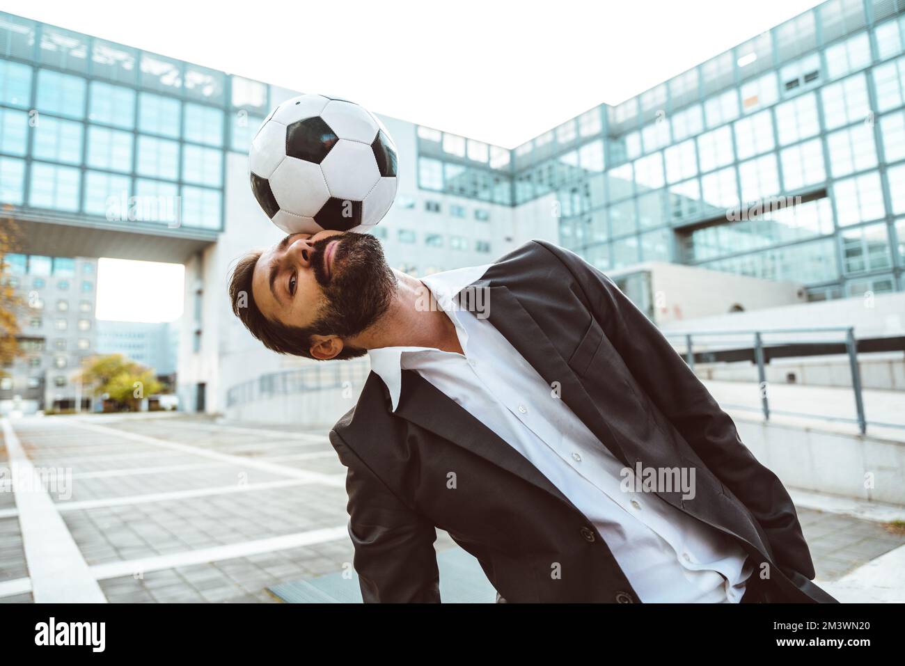 Bild eines Geschäftsmanns und Freispielers, der mit dem Ball auf der Straße Tricks macht. Konzept über Sport- und Geschäftsleute Stockfoto