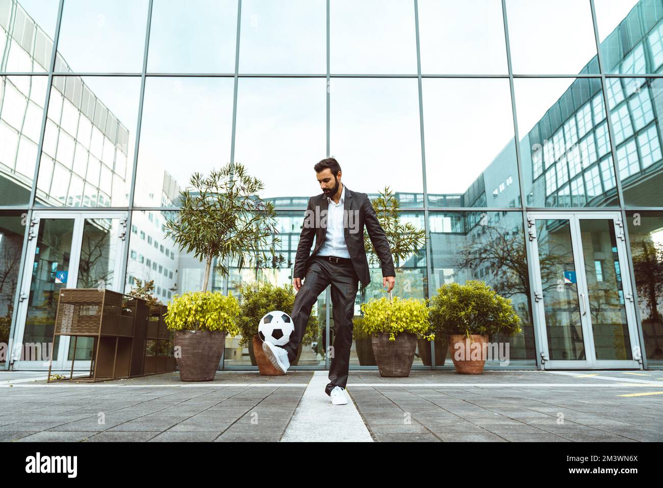Bild eines Geschäftsmanns und Freispielers, der mit dem Ball auf der Straße Tricks macht. Konzept über Sport- und Geschäftsleute Stockfoto