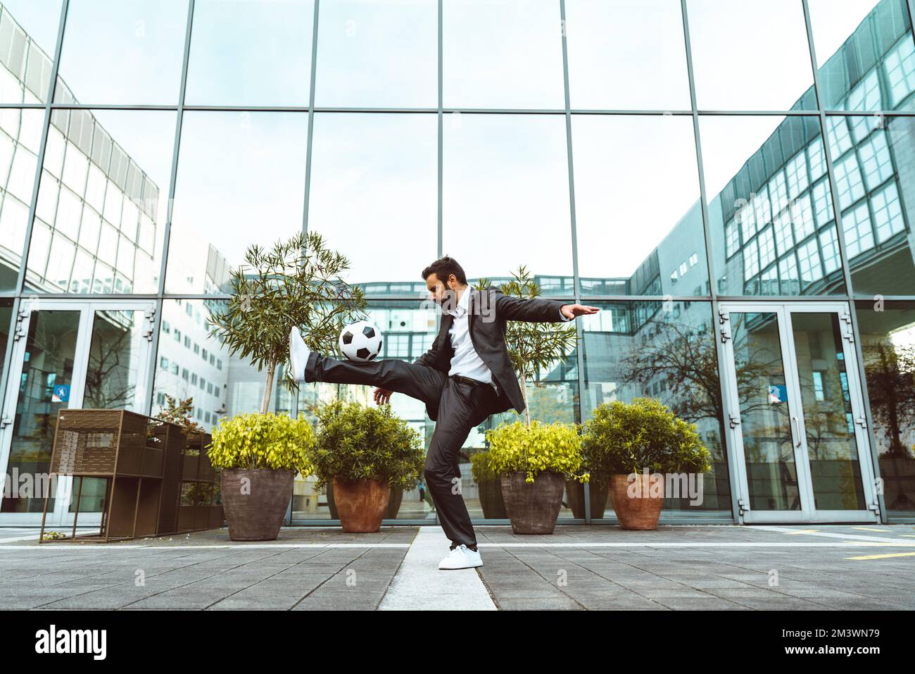 Bild eines Geschäftsmanns und Freispielers, der mit dem Ball auf der Straße Tricks macht. Konzept über Sport- und Geschäftsleute Stockfoto