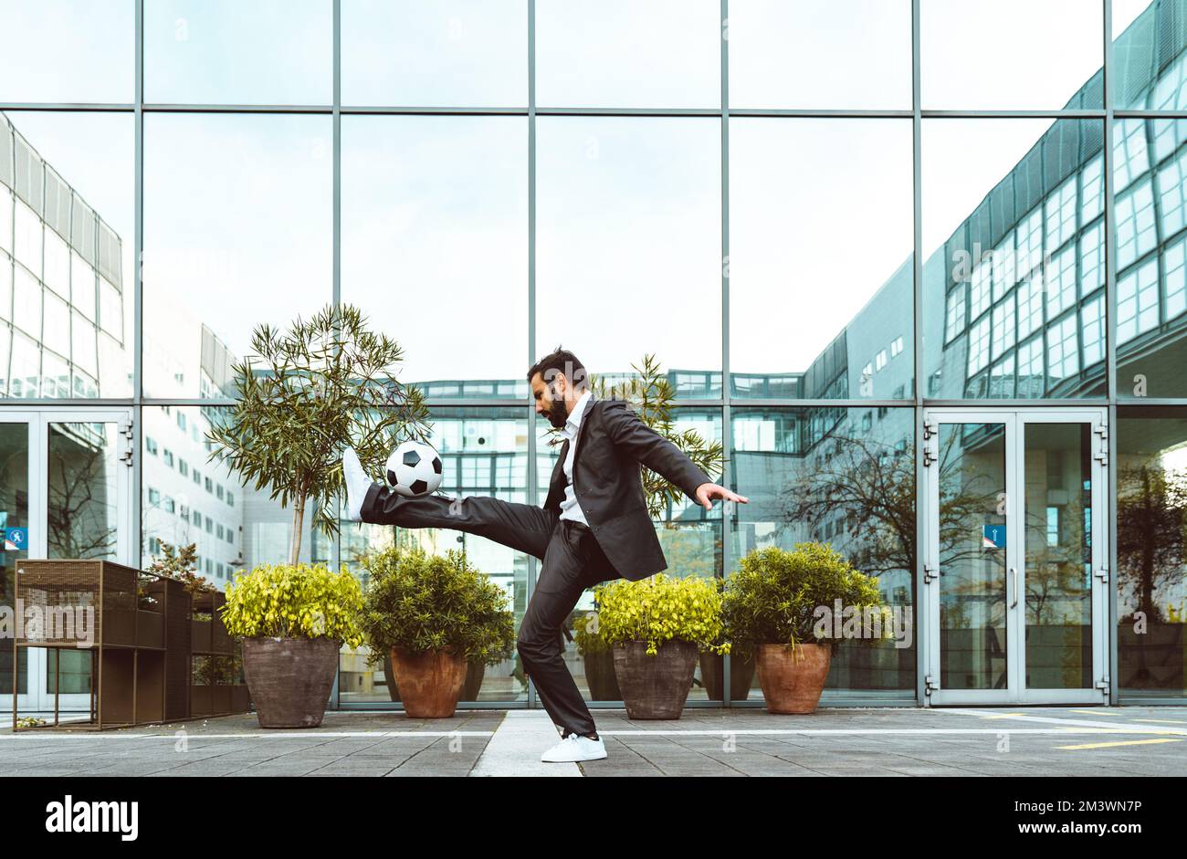 Bild eines Geschäftsmanns und Freispielers, der mit dem Ball auf der Straße Tricks macht. Konzept über Sport- und Geschäftsleute Stockfoto