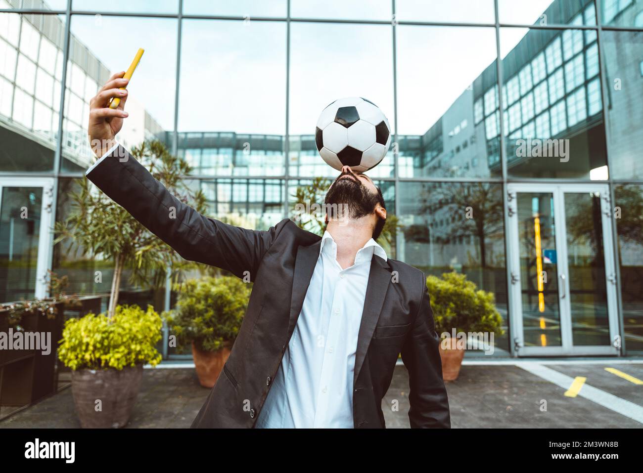 Bild eines Geschäftsmanns und Freispielers, der mit dem Ball auf der Straße Tricks macht. Konzept über Sport- und Geschäftsleute Stockfoto