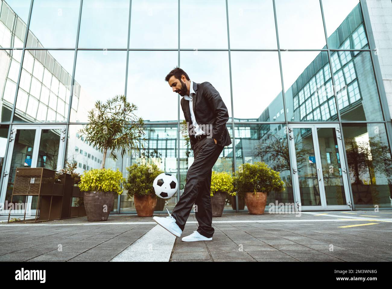 Bild eines Geschäftsmanns und Freispielers, der mit dem Ball auf der Straße Tricks macht. Konzept über Sport- und Geschäftsleute Stockfoto