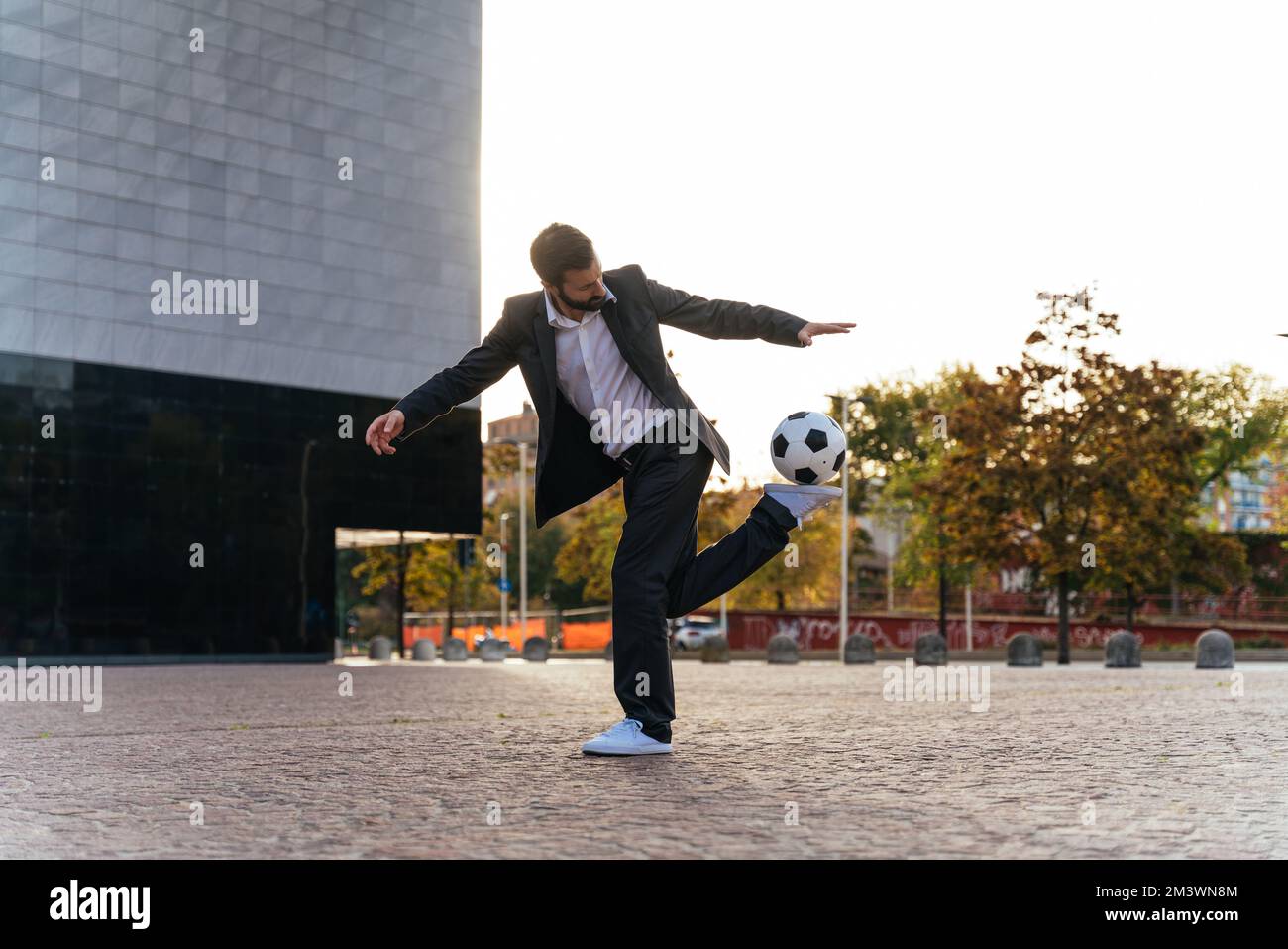 Bild eines Geschäftsmanns und Freispielers, der mit dem Ball auf der Straße Tricks macht. Konzept über Sport- und Geschäftsleute Stockfoto