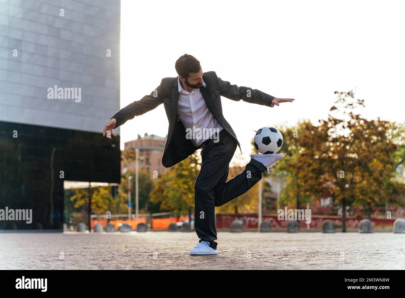 Bild eines Geschäftsmanns und Freispielers, der mit dem Ball auf der Straße Tricks macht. Konzept über Sport- und Geschäftsleute Stockfoto