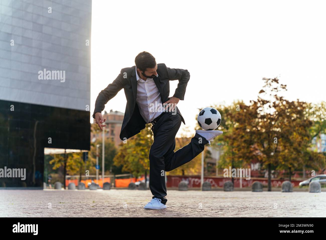 Bild eines Geschäftsmanns und Freispielers, der mit dem Ball auf der Straße Tricks macht. Konzept über Sport- und Geschäftsleute Stockfoto